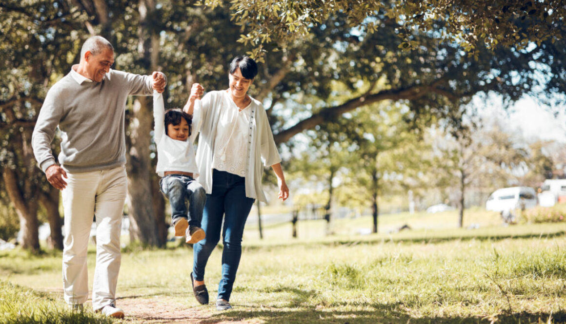 Happy, holding hands and grandparents with child in park for playing, love and support. Swing, smile and freedom with family walking on nature path for fun, summer vacation and happiness together