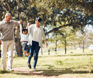 Happy, holding hands and grandparents with child in park for playing, love and support. Swing, smile and freedom with family walking on nature path for fun, summer vacation and happiness together