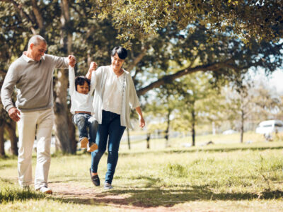 Happy, holding hands and grandparents with child in park for playing, love and support. Swing, smile and freedom with family walking on nature path for fun, summer vacation and happiness together