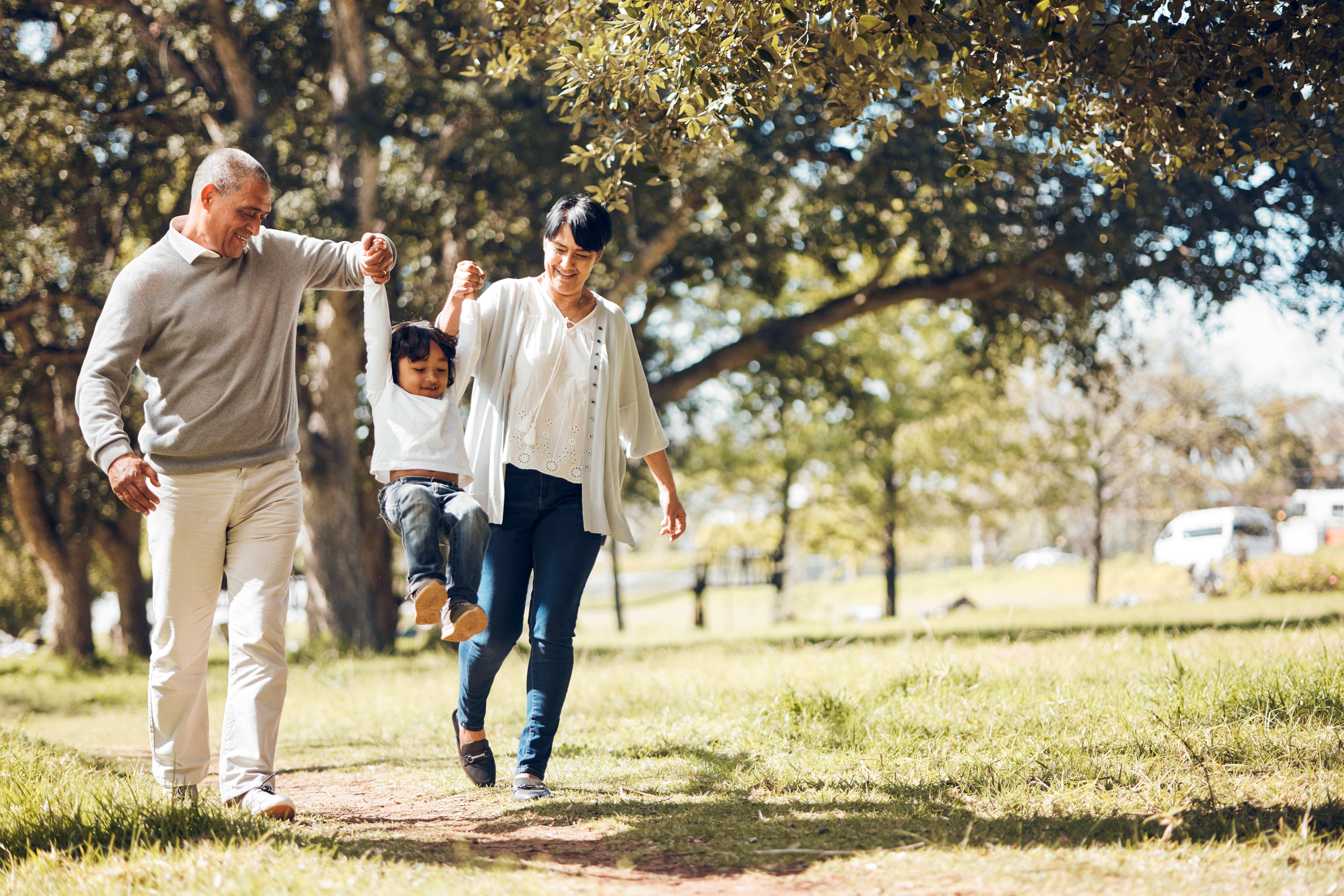 Happy, holding hands and grandparents with child in park for playing, love and support. Swing, smile and freedom with family walking on nature path for fun, summer vacation and happiness together