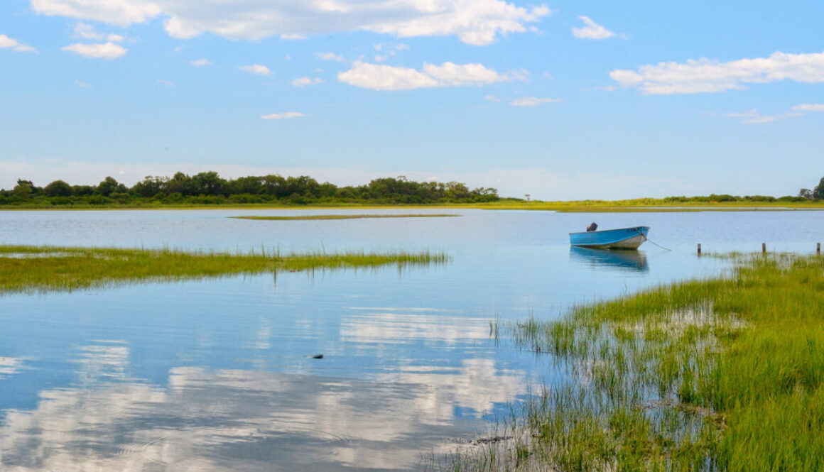 Tranquil view Niantic Connecticut salt marsh in summer with blue sky and blue boat reflections of cumulus clouds in still water with copy space, saltwater tidal marsh, East Lyme, New England scenic