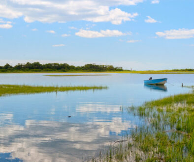 Tranquil view Niantic Connecticut salt marsh in summer with blue sky and blue boat reflections of cumulus clouds in still water with copy space, saltwater tidal marsh, East Lyme, New England scenic