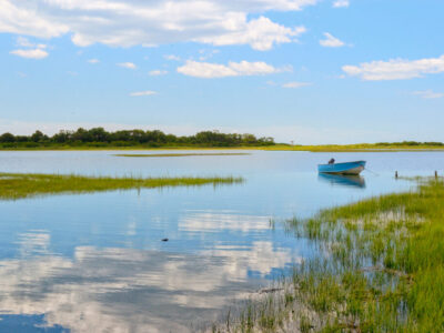 Tranquil view Niantic Connecticut salt marsh in summer with blue sky and blue boat reflections of cumulus clouds in still water with copy space, saltwater tidal marsh, East Lyme, New England scenic