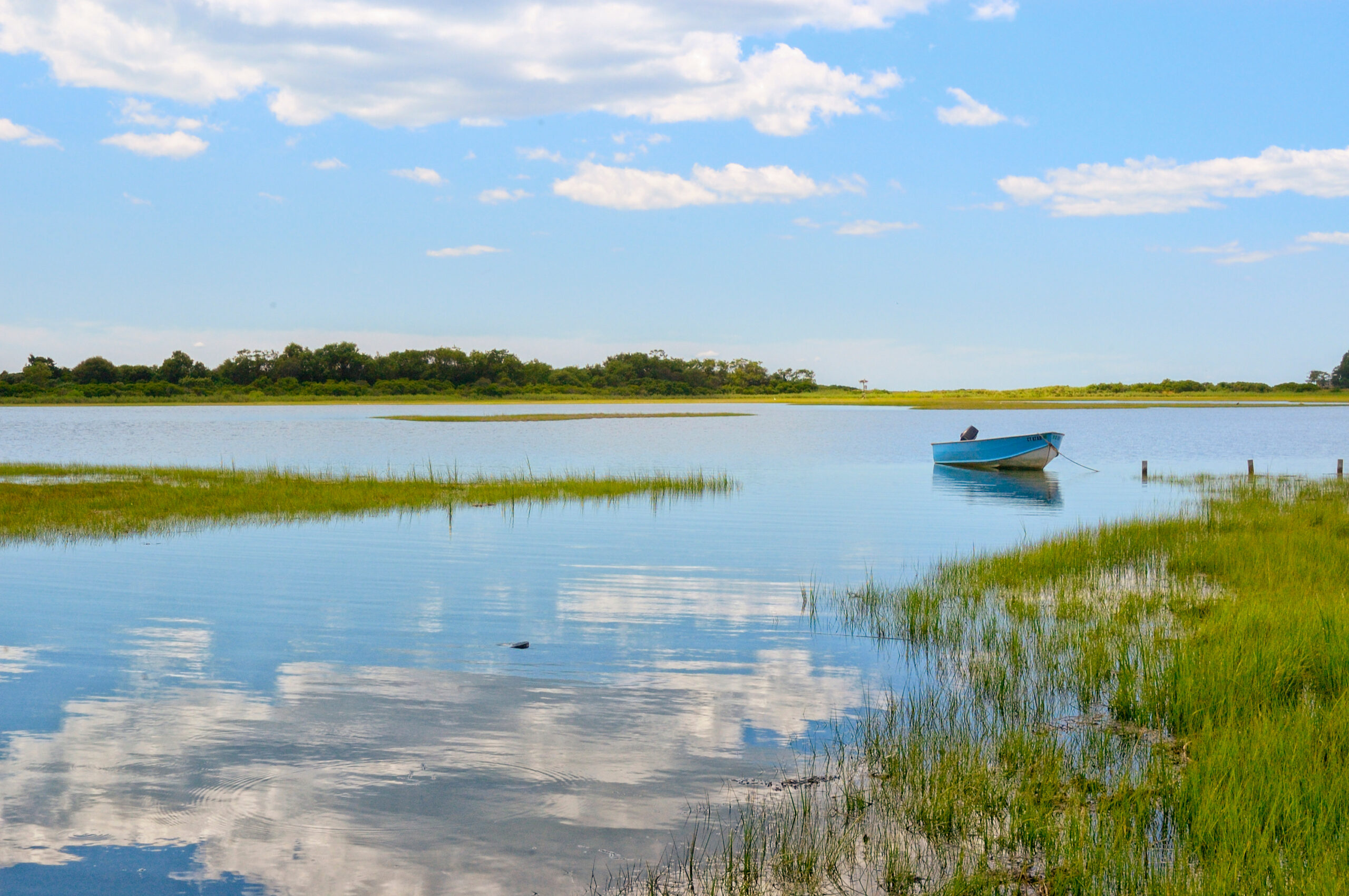 Tranquil view Niantic Connecticut salt marsh in summer with blue sky and blue boat reflections of cumulus clouds in still water with copy space, saltwater tidal marsh, East Lyme, New England scenic